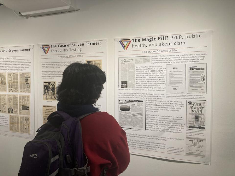 Jacqueline Ojeda Mendez stands reading a poster compilation of SGN headlines at the Viking Union Gallery on Jan. 14, 2025, in Bellingham, Wash. Mendez said that they liked how the exhibit was structured chronologically and focused on key moments in queer history. // Photo by McKenna Kilayko